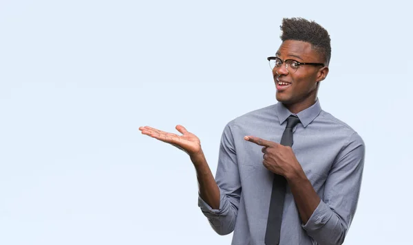 Young african american business man over isolated background amazed and smiling to the camera while presenting with hand and pointing with finger.