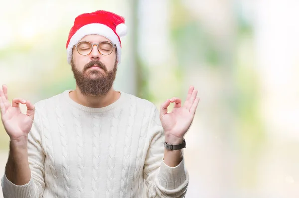 孤立した背景にクリスマスの帽子とメガネを着て若い白人男リラックスして瞑想の指ジェスチャーをやって閉じた目と笑顔します ヨガの概念 — ストック写真