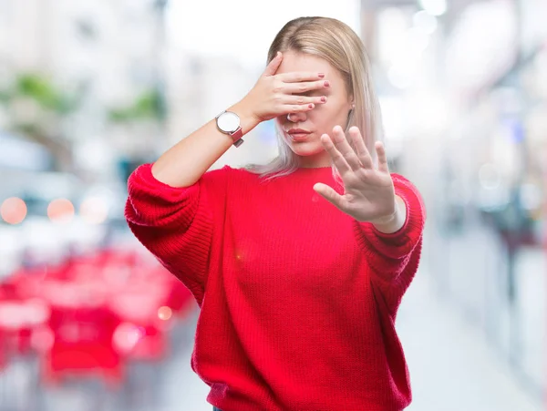 Young blonde woman wearing winter sweater over isolated background covering eyes with hands and doing stop gesture with sad and fear expression. Embarrassed and negative concept.