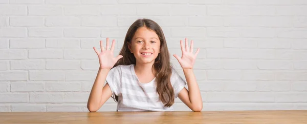 年轻的西班牙裔孩子坐在家里的桌子上显示和指着手指十号同时微笑自信和快乐 — 图库照片