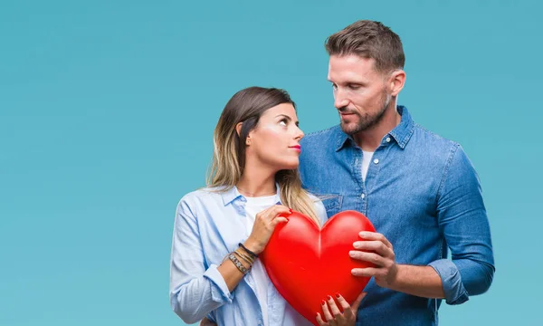 年轻夫妇在爱持有红色心脏在孤立的背景与自信的表情在聪明的脸思考严重 — 图库照片
