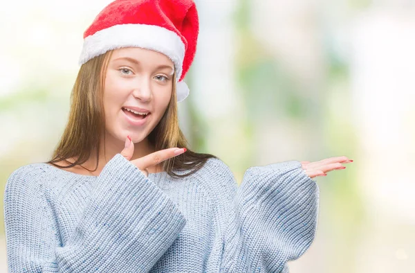 年轻美丽的白人妇女戴着圣诞节帽子在孤立的背景惊讶和微笑的相机 而提出与手和手指指向 — 图库照片