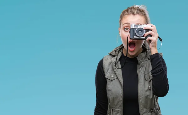 Young blonde woman taking pictures using vintage camera over isolated background scared in shock with a surprise face, afraid and excited with fear expression