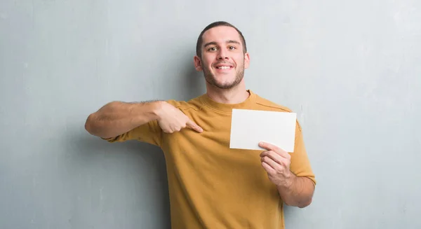 Joven Caucásico Hombre Sobre Gris Grunge Pared Celebración Tarjeta Blanco — Foto de Stock