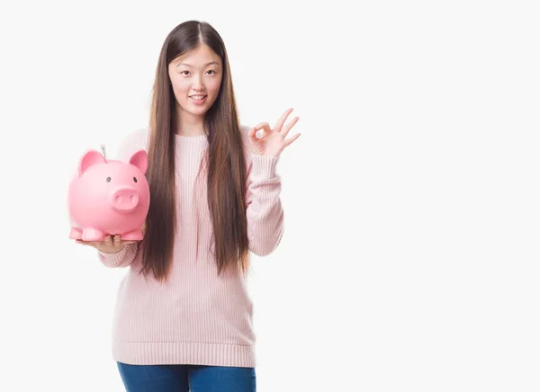 優秀なシンボルの指で サインをして貯金を保持分離の背景の上の若い中国の女性 — ストック写真