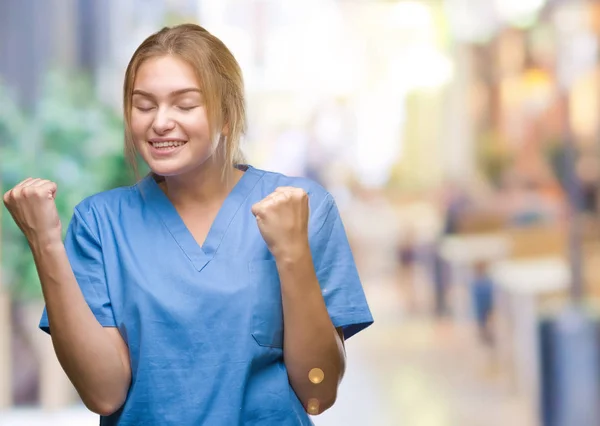 若い白人の看護師女性非常に幸せと興奮の腕を上げ 勝者のジェスチャを行う分離の背景の上の外科医の制服を着て笑顔で成功のために叫んで お祝いのコンセプト — ストック写真