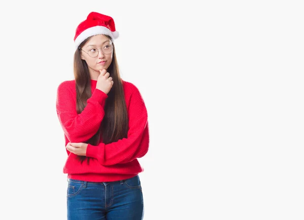 あごを考えて質問 物思いにふける式に手でクリスマス帽子をかぶっている孤立の背景の上の若い中国の女性 思いやりのある顔をして笑っています 疑いのコンセプト — ストック写真
