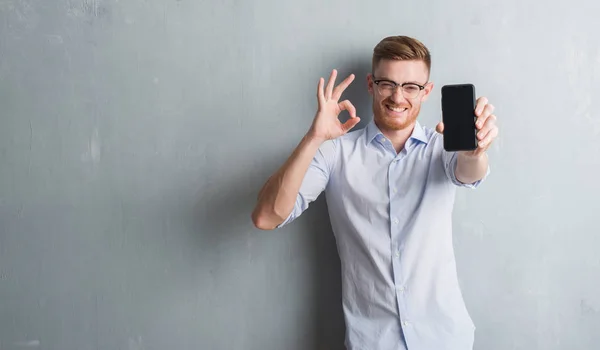 Joven Pelirrojo Sobre Pared Grunge Gris Que Muestra Pantalla Blanco —  Fotos de Stock