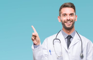 Kameraya bakarak yan el ve parmak ile işaret eden genç yakışıklı Doktor adam yüzünde kocaman bir gülümseme ile izole arka plan üzerinde.