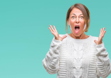 Üzerinde kış kazak giyen orta yaş üst düzey İspanyol kadın deli kutluyor arka plan izole ve başarı için kaldırdı kollarını açarak hayrete ve heyecanlı çığlık gözleri açık. Kazanan kavramı