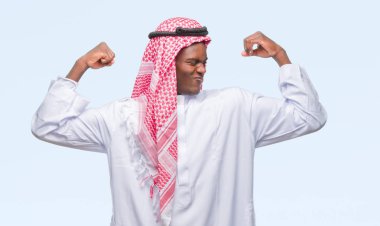 Geleneksel keffiyeh kol kasları gururlu gülümseyen gösterilen izole arka plan üzerinde giyen genç Arapça Afrika adam. Fitness kavramı.
