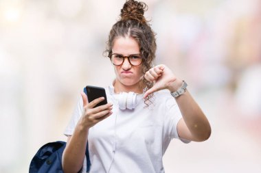 Sırt çantası, kulaklık ve akıllı telefon üzerinde giyen genç esmer öğrenci kız arka plan kızgın yüzü, eksi işareti aşağı antipati başparmak ile gösterilen, ret kavramı ile izole