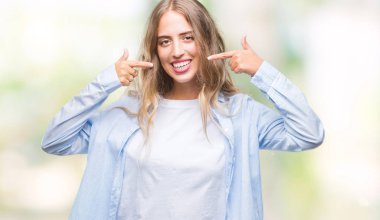 Güzel sarışın genç kadın kendine güvenen gösterilen ve işaret parmakları diş ve ağız ile gülümseyen izole arka plan üzerinde. Sağlık kavramı.