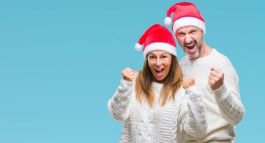 Orta yaş İspanyol çift üzerinde Noel şapka arka plan çok mutlu ve heyecanlı gülümseyen ve başarı için çığlık kaldırdı, silah ile kazanan jest yapıyor izole. Kutlama kavramı.