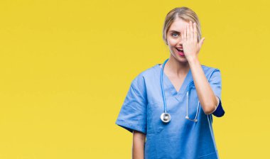 Genç güzel sarışın doktor cerrah hemşire kadın el yüz ve sürpriz duygu kendinden emin gülümseme ile tek gözüyle kapsayan izole arka plan.