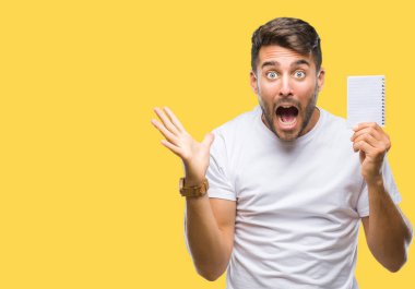 Kocaman bir gülümseme ile çığlık zaferini kutluyor ve ellerini kaldırdı izole arka plan çok mutlu ve heyecanlı, kazanan ifade üzerinde defter tutan genç yakışıklı adam