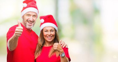 Orta yaş İspanyol çift hareketi el ile mutlu yaşasın yapıyor izole arka plan üzerinde Noel şapka giyiyor. Kameraya bakarak başarı gösteren ile ifade onaylama.