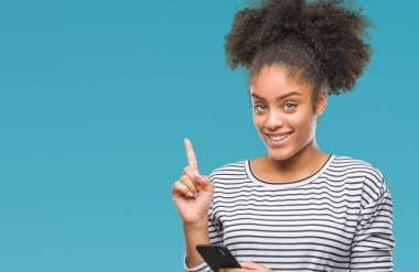 Genç afro Amerikalı kadın manifatura Smartphone izole arka bir fikir ya da soru işaret parmağı gülen yüz, bir numara ile sürpriz üzerinde kullanma