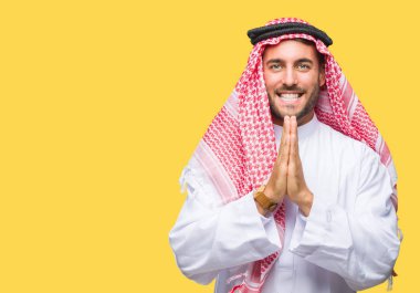 Keffiyeh birlikte AF emin gülümseyen için soran ellerle dua izole arka plan üzerinde giyen genç yakışıklı adam.