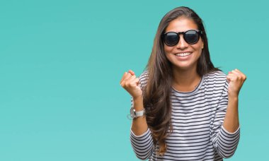 Genç güzel Arap kadın izole arka plan kutlama üzerinde güneş gözlüğü takıyor şaşırttı ve başarı için kaldırdı kollarını açarak hayret ve gözleri açık. Kazanan kavramı.