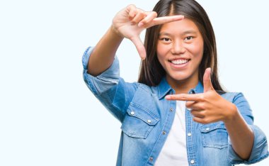 Genç Asyalı kadın elle yapma çerçeve ve parmakları ile mutlu yüz gülümseyen izole arka plan üzerinde. Yaratıcılık ve Fotoğrafçılık kavramı.