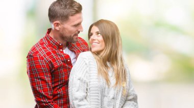 Aşık üzerinde kış kazak giyen genç çift arka plan uzak tarafına gülümseme ile yüzünde, doğal ifade arıyorum izole. Kendine güvenen gülüyor.