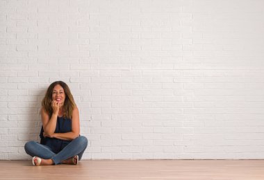 Tırnak ısırma dudaklarından eller orta yaş İspanyol kadın stresli ve gergin ile beyaz tuğla duvarın üzerinden yere oturma. Anksiyete sorunu.