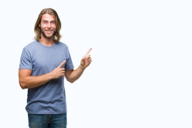 Gülümseyen ve iki elleri ve parmakları ile tarafına işaret kamera bakarak izole arka plan üzerinde uzun saçlı yakışıklı delikanlı.