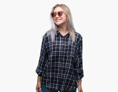 Sarışın genç kadın uzak tarafına yüzünde, doğal ifade gülümseme ile seyir izole arka plan üzerinde güneş gözlüğü takıyor. Kendine güvenen gülüyor.