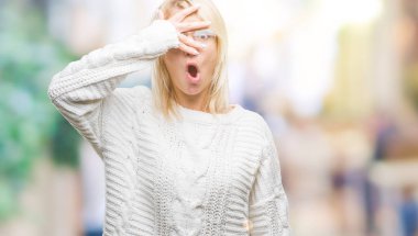 Mahcup ifadeyle parmaklarımın arasından seyir kış kazak ve gözlük yüz ve gözler el ile kapsayan şok izole arka plan bakmak üzerinde giyen genç güzel sarışın kadın.