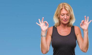 Orta yaş sarışın kadın izole arka plan üzerinde dinlenmek ve gülümseyen gözlerle parmak ile meditasyon jest yapıyor kapalı. Yoga kavramı.