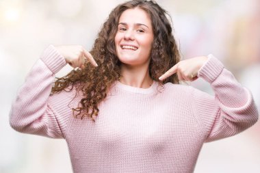 Yüzünde gülümseme ile kendinden emin görünüyorsun, kendini gururlu ve mutlu parmakları ile işaret izole arka plan üzerinde pembe kış kazak giyen güzel esmer kıvırcık saçlı Genç kız.