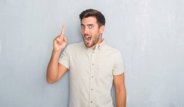 Yakışıklı genç gri grunge üzerinde başarılı fikir giyen Yaz gömlek işaret parmağı duvar. Çıktıktan ve mutlu. Bir numara.