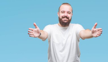 Sarılmak için kollarını açarak gülümseyerek kameraya bakarak izole arka plan üzerinde rahat t-shirt giyen genç beyaz hipster adam. Neşeli ifade kucaklayan mutluluk.