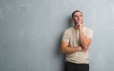 Beyaz delikanlı çene düşünme hakkında soru, dalgın ifade üzerine el ile gri grunge duvarın üzerinden. Düşünceli yüzüyle gülümsüyor. Şüphe kavramı.