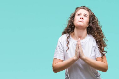 Güzel esmer kıvırcık saçlı Genç kız yalvarıyor ve umut ifade yüzünde çok duygusal ve endişe ile birlikte elleriyle dua izole arka plan üzerinde rahat t-shirt giyiyor. Bağışlanmak. Din kavramı.