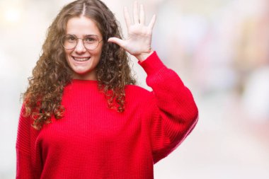 Gösterilen ve parmakları ile işaret izole arka plan üzerinde gözlük ve kış kazak giyen güzel esmer kıvırcık saçlı Genç kız kendinden emin ve mutlu gülümseyerek süre beş numara.