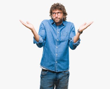 Üzerinde gözlük takan yakışıklı İspanyol model adam arka plan clueless ve şaşkın bir ifadeyle kollar ve eller kaldırdı izole. Şüphe kavramı.