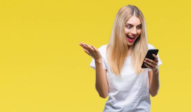 Smartphone üzerinde kocaman bir gülümseme ile çığlık zaferini kutluyor ve ellerini kaldırdı izole arka plan çok mutlu ve heyecanlı, kazanan ifade kullanan genç güzel sarışın kadın