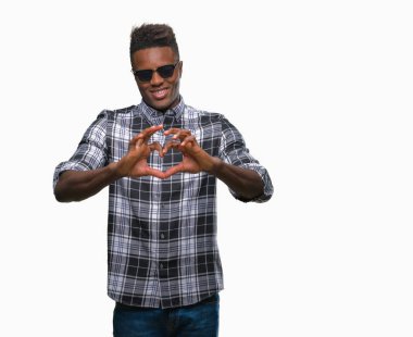 Genç Afro-Amerikan adam aşık kalp simgesi ve elleriyle şekil gösteren gülümseyen izole arka plan üzerinde güneş gözlüğü takıyor. Romantik kavramı.
