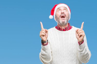 Noel şapka izole arka plan üzerinde orta yaş ağarmış komuta sizde hayrete ve yukarıya bakıyor ve parmakları ile işaret ve silah kaldırdı şaşırttı.