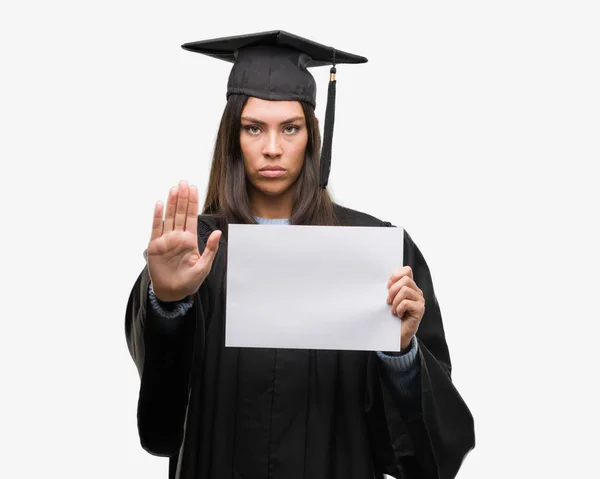 若いヒスパニック女性着て卒業制服防衛ジェスチャー 深刻な自信を持って式に一時停止の標識をやって開いた手に卒業証書用紙を保持 — ストック写真