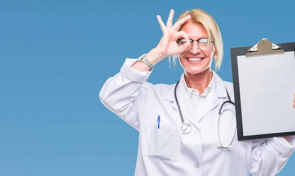 中年金发医生妇女持有剪贴板在孤立的背景与快乐的脸微笑做 标志与手在眼睛看通过手指 — 图库照片