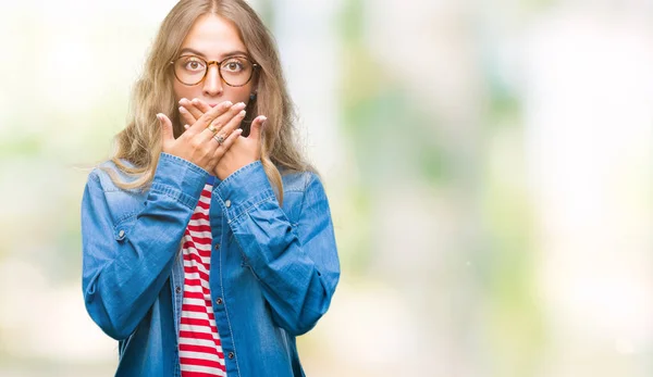 美丽的年轻金发女子戴着眼镜在孤立的背景震惊地覆盖口与手错误 秘密概念 — 图库照片