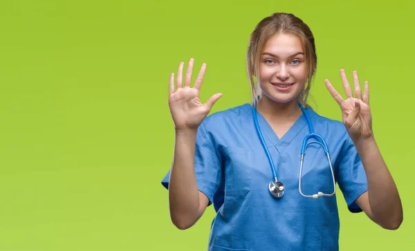 年轻的白种人医生妇女穿外科医生制服在孤立的背景显示和指向与手指数字九同时微笑自信和快乐 — 图库照片
