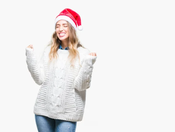 笑顔と成功のために叫んで 上クリスマス帽子身に着けている美しい若いブロンドの女性は非常に幸せと興奮の腕を上げ 勝者のジェスチャを行う背景を分離しました お祝いのコンセプト — ストック写真