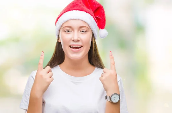若い美しい白人女性隔離された背景にクリスマスの帽子をかぶってびっくり驚いて見上げると指で指していると腕を上げた — ストック写真