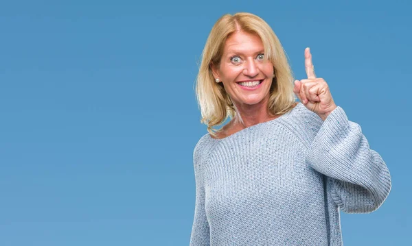 Middle age blonde woman wearing winter sweater over isolated background pointing finger up with successful idea. Exited and happy. Number one.