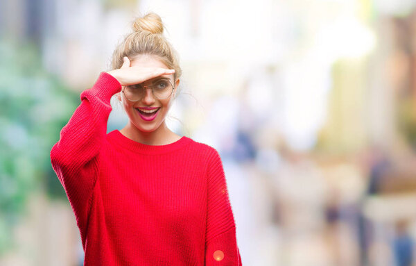 Young beautiful blonde woman wearing red sweater and glasses over isolated background very happy and smiling looking far away with hand over head. Searching concept.