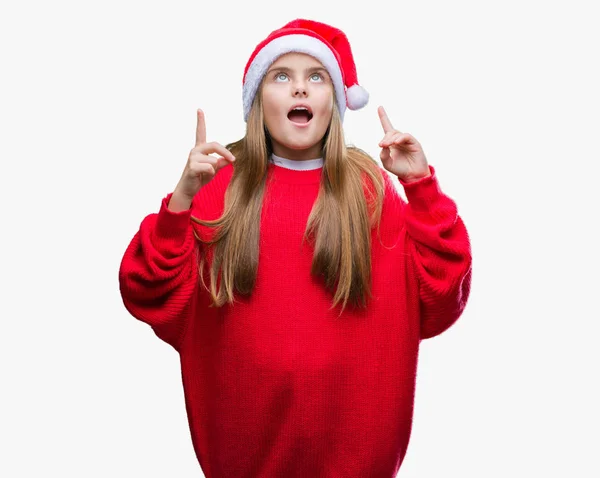 孤立した背景にクリスマスの帽子を着て美しい少女びっくり驚いて見上げると指で指していると腕を上げた — ストック写真